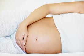 A pregnant woman laying in bed with her hands on her stomach.