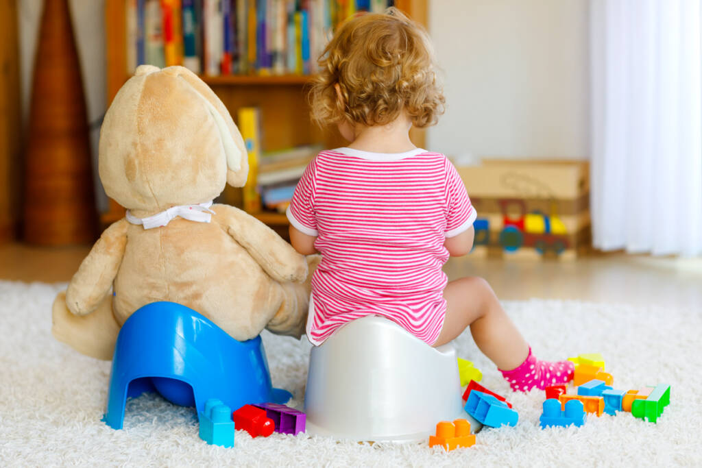 A toddler sitting on top of a potty next to a teddy bear.