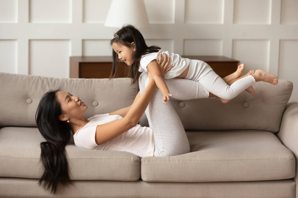 A woman and child are playing on the couch.